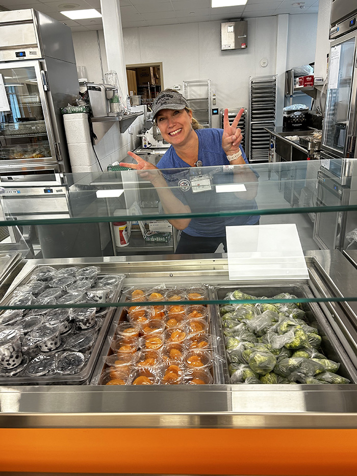 Food Services worker smiling behind healthy lunch selections