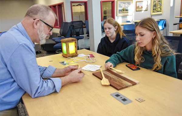Principal Scott Hemlin checks out kitchenware, spoons, and a cutting board made by Logan Burke, right, and a stained glass electric lantern made by Megan Parse.