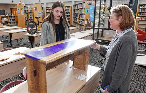 Student Madilyn Moore shows the epoxy resin table she made out of walnut to educator Maureen Donovan.